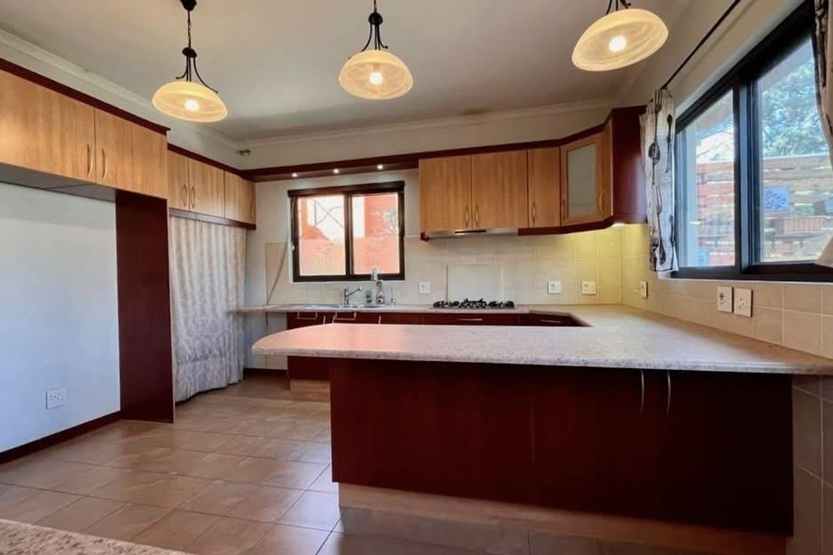 A spacious kitchen featuring built-in cabinetry, laminate countertops, a gas hob, and tiled flooring, offering a functional layout with ample storage space.
