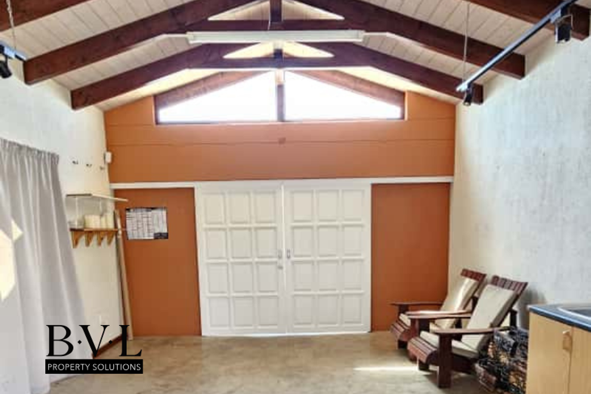Spacious living area featuring high vaulted timber-beamed ceilings, large double doors, and polished concrete flooring, offering a bright and airy atmosphere.