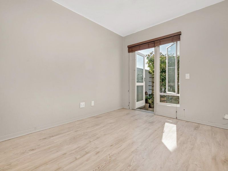 A bright, empty bedroom featuring light-toned laminate flooring and a glass-paneled door providing direct access to an outdoor area.