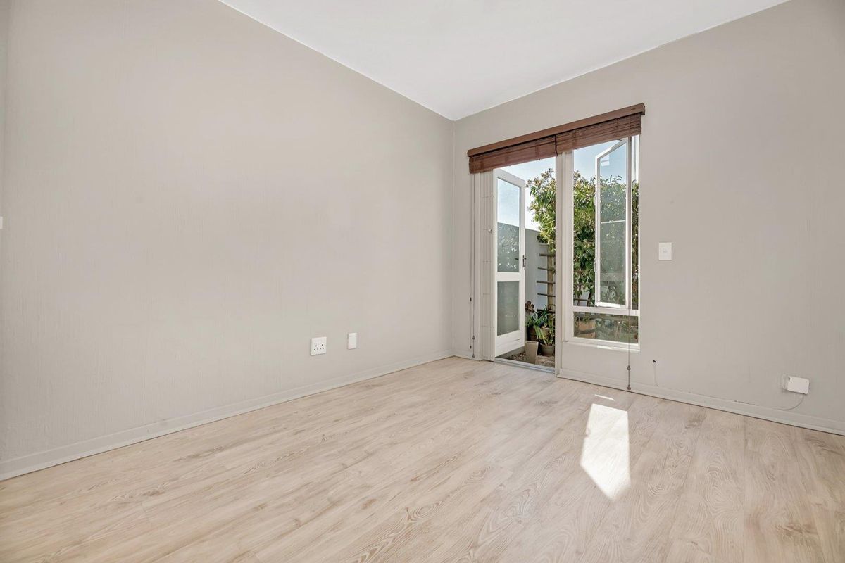 A bright, empty bedroom featuring light-toned laminate flooring and a glass-paneled door providing direct access to an outdoor area.