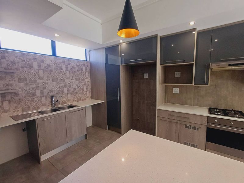 Modern kitchen featuring sleek grey and wood-tone cabinetry, stone countertops, integrated gas hob, oven, and extractor fan with contemporary tiled splashback.
