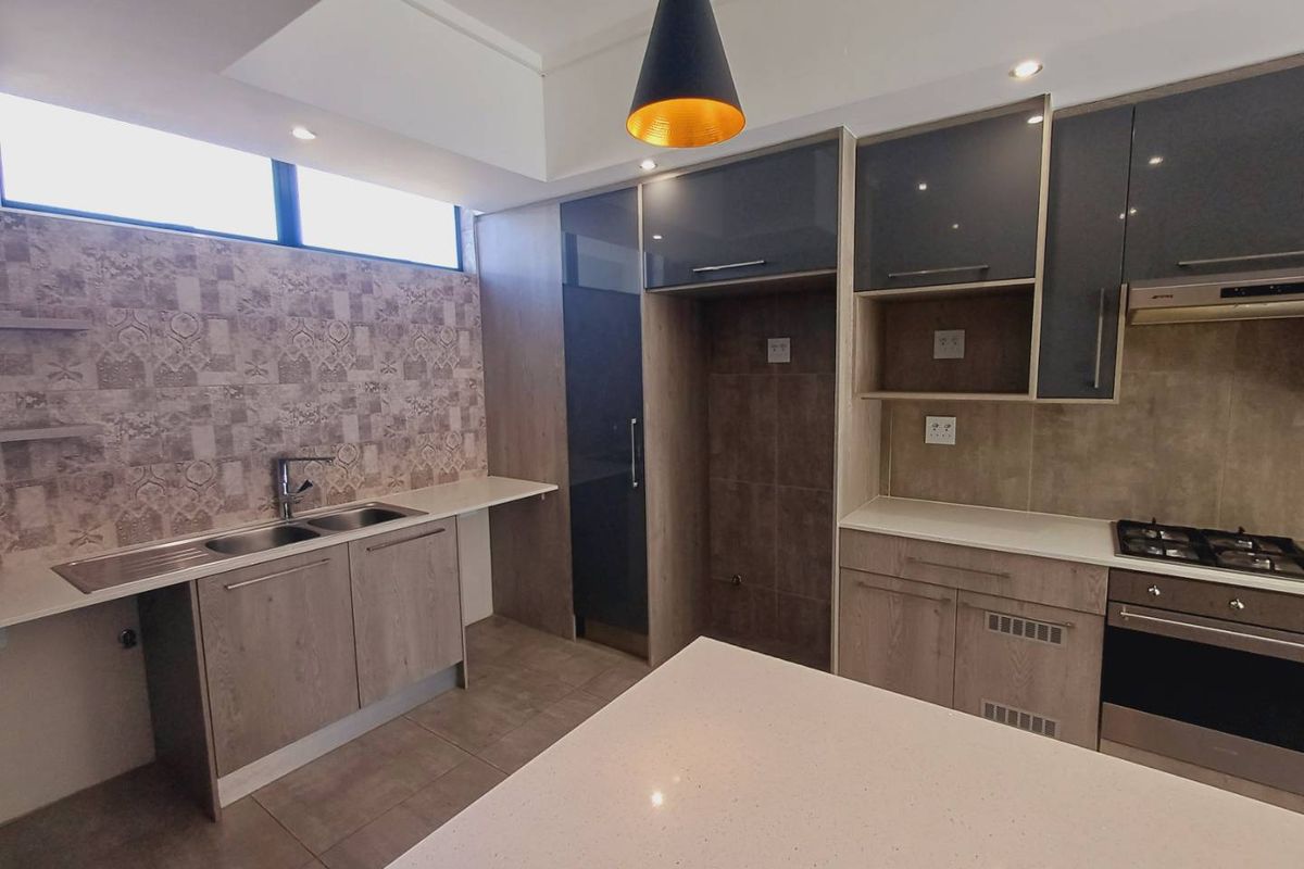 Modern kitchen featuring sleek grey and wood-tone cabinetry, stone countertops, integrated gas hob, oven, and extractor fan with contemporary tiled splashback.