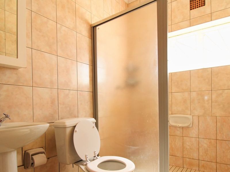A functional bathroom featuring a pedestal basin, toilet, and a shower enclosure with tiled walls and flooring.