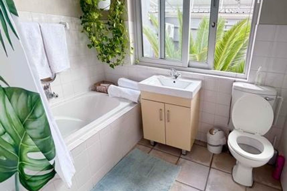 A functional bathroom featuring a bathtub, vanity with integrated basin, toilet, and tiled finishes with natural light from a large window.