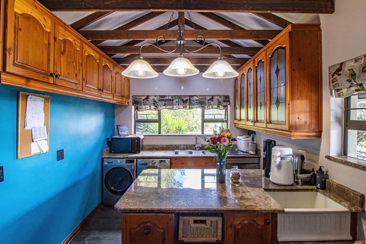 A rustic kitchen featuring warm wooden cabinetry, granite countertops, exposed timber ceiling beams, and a combination of double basin and apron front sinks.