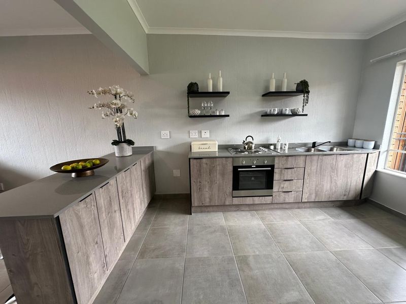 Modern kitchen featuring wood-look cabinetry, stone countertops, integrated oven and hob, and sleek floating shelving in a neutral, contemporary design.
