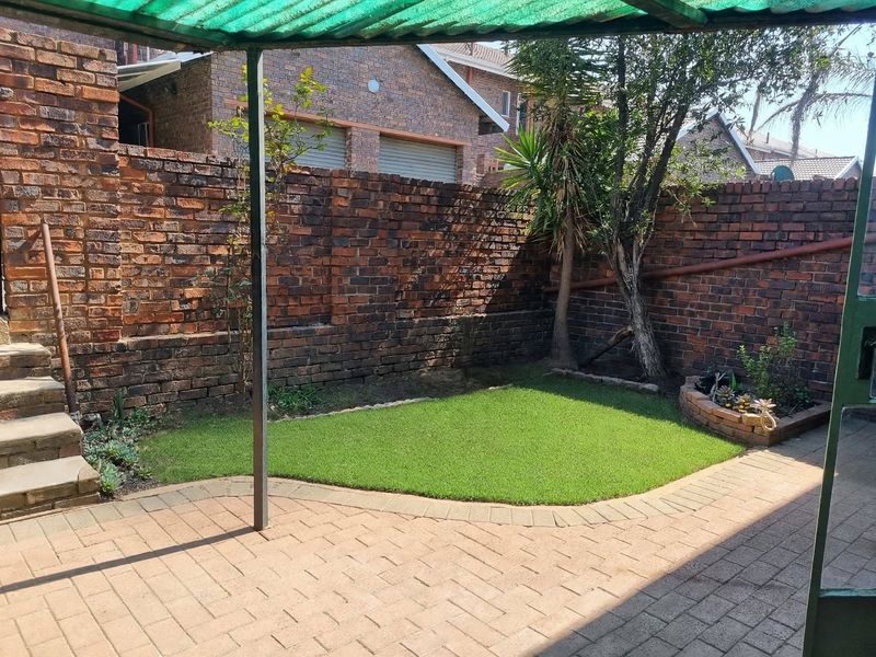 A private rear courtyard featuring a paved patio area, a small lawn, and a covered outdoor space enclosed by brick boundary walls.