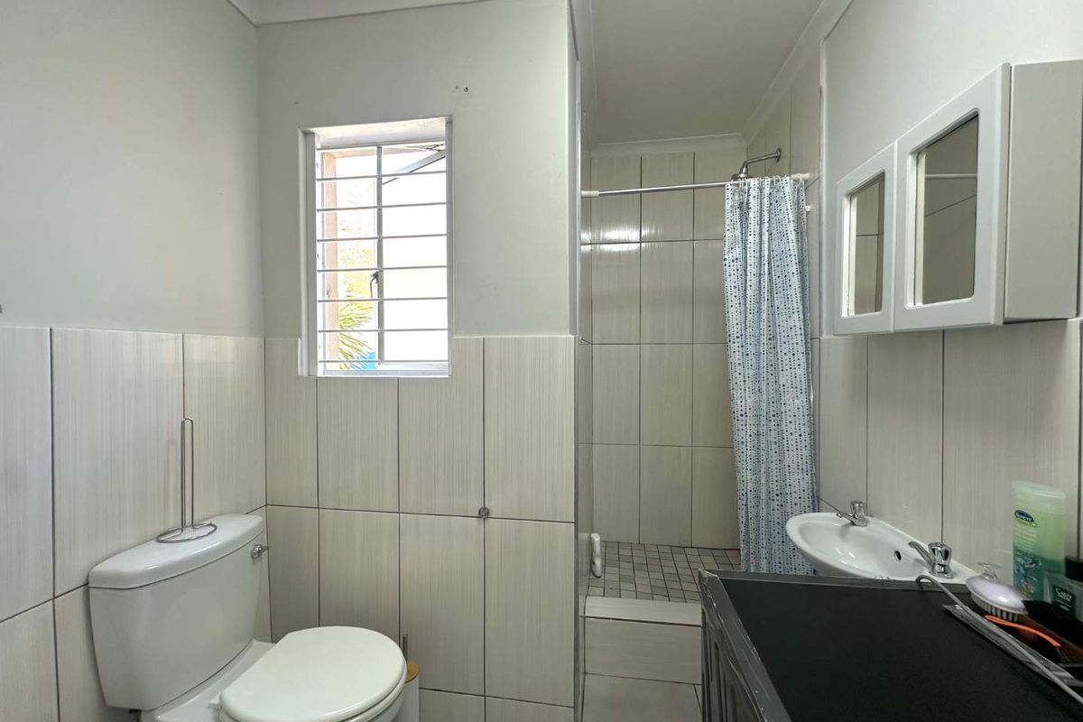 A functional bathroom featuring a walk-in shower, wall-mounted basin, and toilet, finished with neutral wall tiling and a security-barred window.