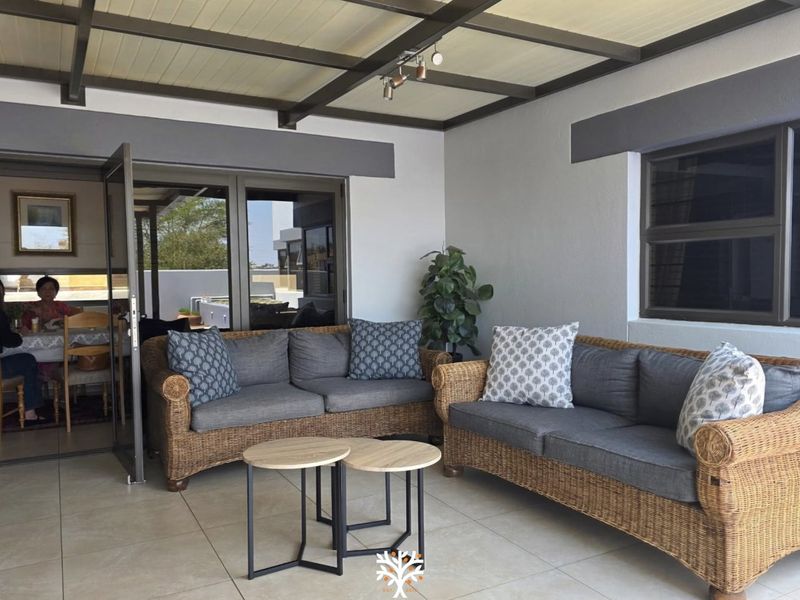 A well-maintained covered patio featuring tiled flooring, exposed beam ceiling, and aluminium framed doors leading to the interior living space.