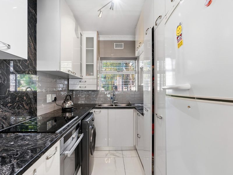 Modern galley-style kitchen featuring high-gloss cabinetry, granite countertops, a double basin sink, and integrated appliances including an oven and hob.