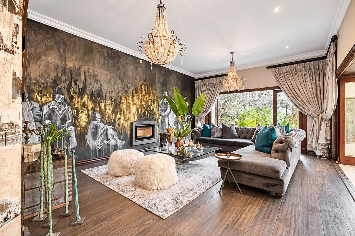 Elegant living room featuring hardwood flooring, a built-in fireplace with artistic wall treatment, crystal chandeliers, and large sliding doors opening to the garden.