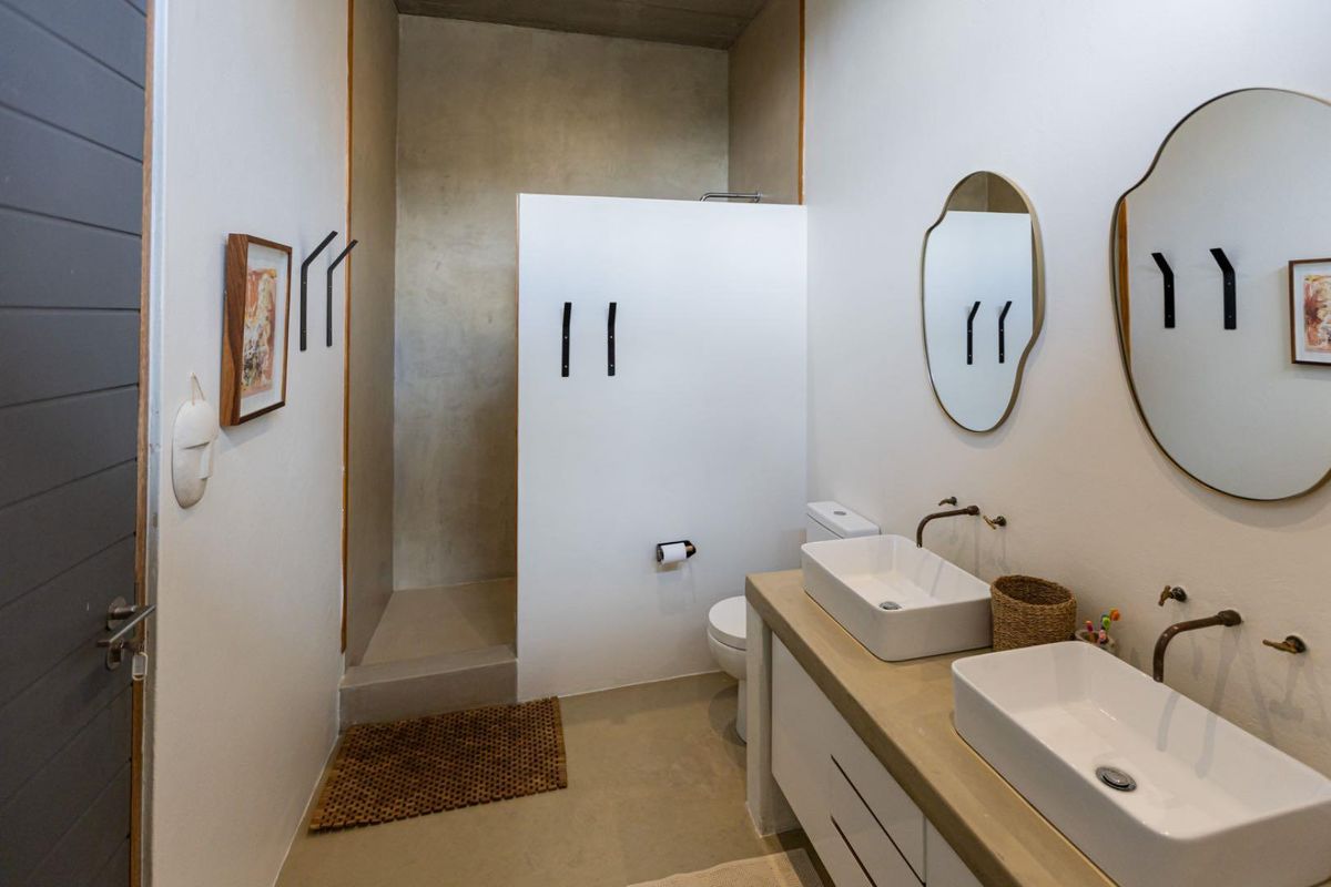 Modern bathroom featuring a double vanity with vessel sinks, wall-mounted faucets, and a walk-in shower with a contemporary concrete-style finish.