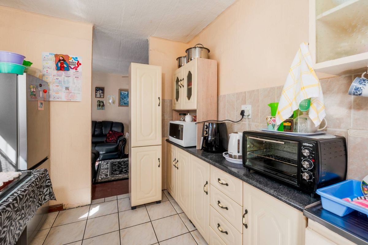 A compact kitchen featuring laminate cabinetry, tiled splashbacks, and tiled flooring, leading into an adjacent living area.