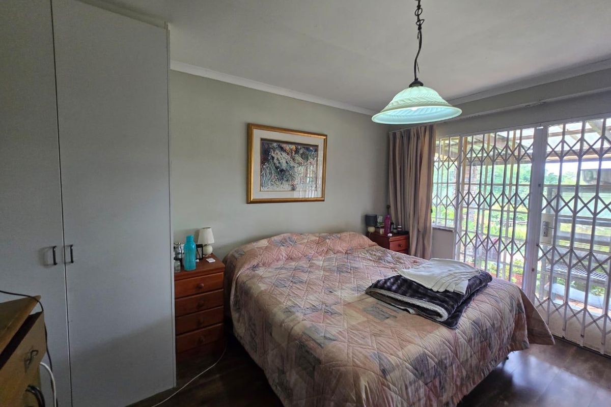 A bedroom featuring built-in cupboards, laminate flooring, and a sliding door with security gate providing access to the outdoors.