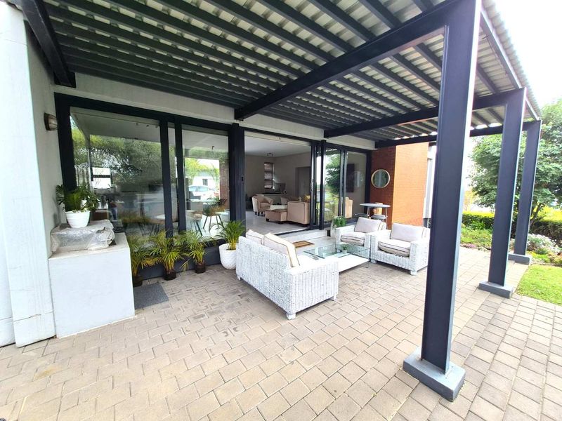 A spacious covered patio featuring a modern metal pergola structure, paved flooring, and large sliding glass doors providing seamless access to the interior living area.