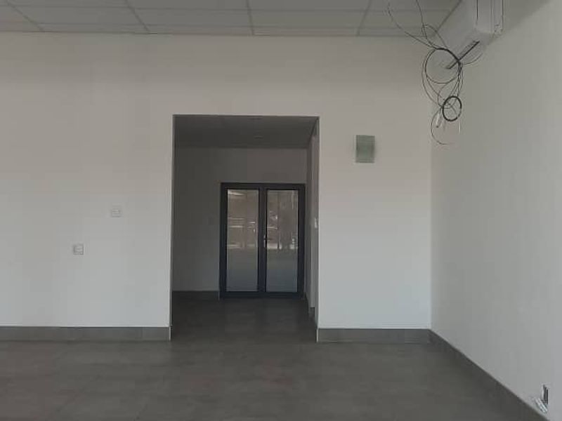 An empty open-plan retail space featuring tiled flooring, a suspended ceiling, and a double glass door entrance.