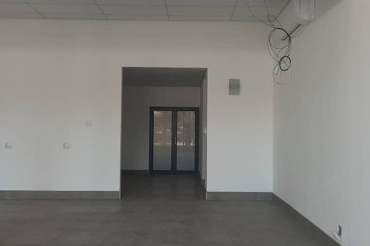 An empty open-plan retail space featuring tiled flooring, a suspended ceiling, and a double glass door entrance.