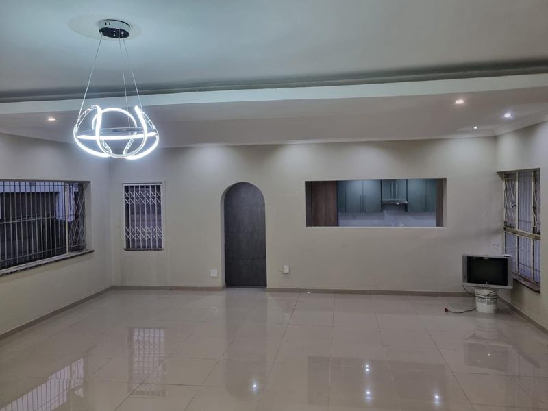 Spacious, open-plan living area featuring polished tile floors, a modern pendant light fixture, and a convenient pass-through window connecting to the kitchen.