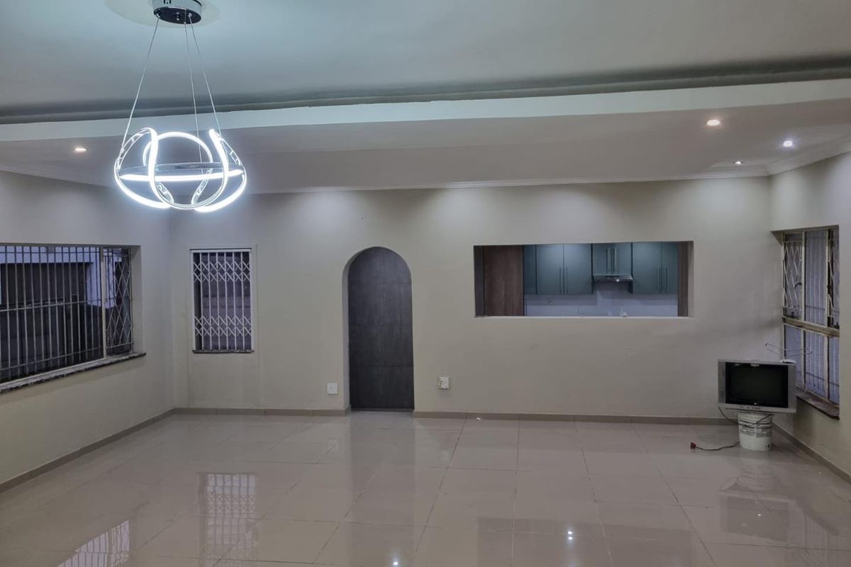 Spacious, open-plan living area featuring polished tile floors, a modern pendant light fixture, and a convenient pass-through window connecting to the kitchen.