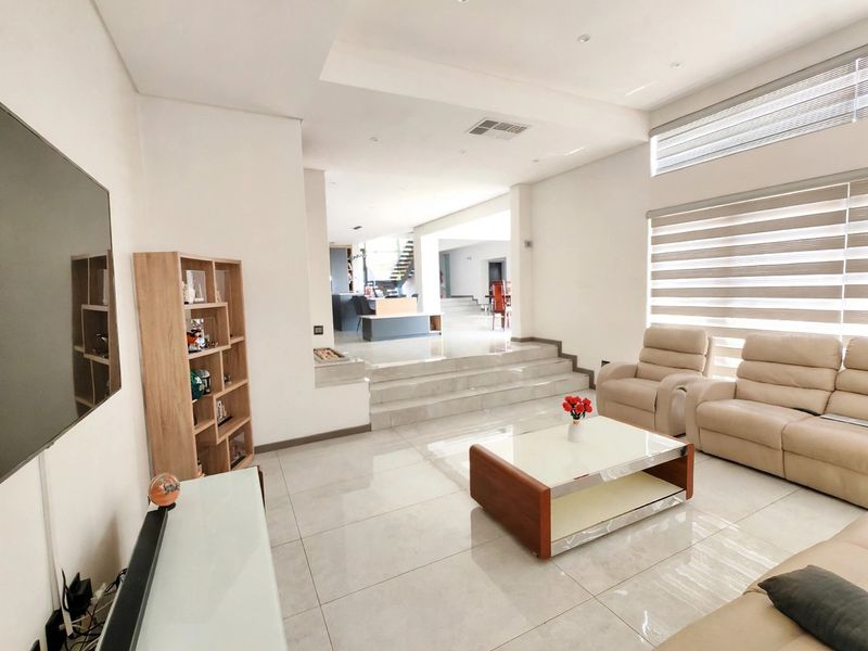 Spacious open-plan living area featuring modern tiled flooring, recessed lighting, and a split-level design leading to the dining and kitchen areas.