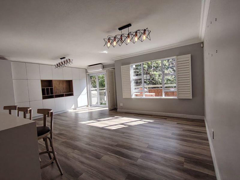 Spacious open-plan living area featuring modern laminate flooring, built-in cabinetry, plantation shutters, and an air conditioning unit, offering a bright and versatile living space.