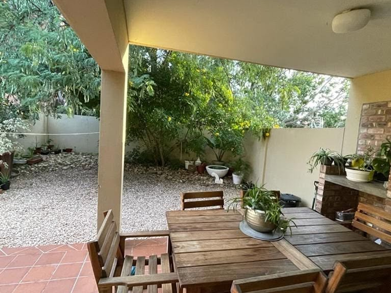A covered patio area featuring tiled flooring and a built-in brick braai, overlooking a private garden space.