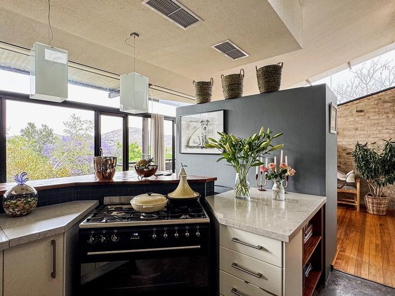 Modern kitchen featuring stone countertops, a gas stove, and timber flooring, with large windows offering scenic views and an open-plan layout.