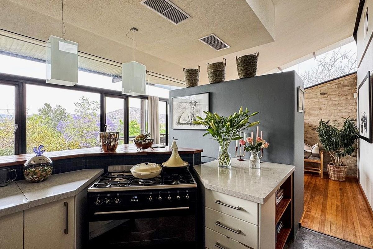 Modern kitchen featuring stone countertops, a gas stove, and timber flooring, with large windows offering scenic views and an open-plan layout.