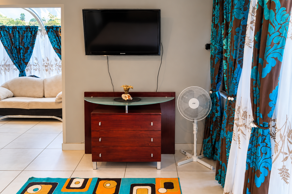 A living room area featuring tiled flooring and a wall-mounted television, with an adjacent view into a secondary lounge space.