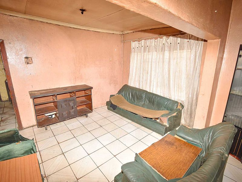 A dated living room featuring ceramic floor tiles and a built-in display cabinet, requiring significant cosmetic updates and wall repairs.