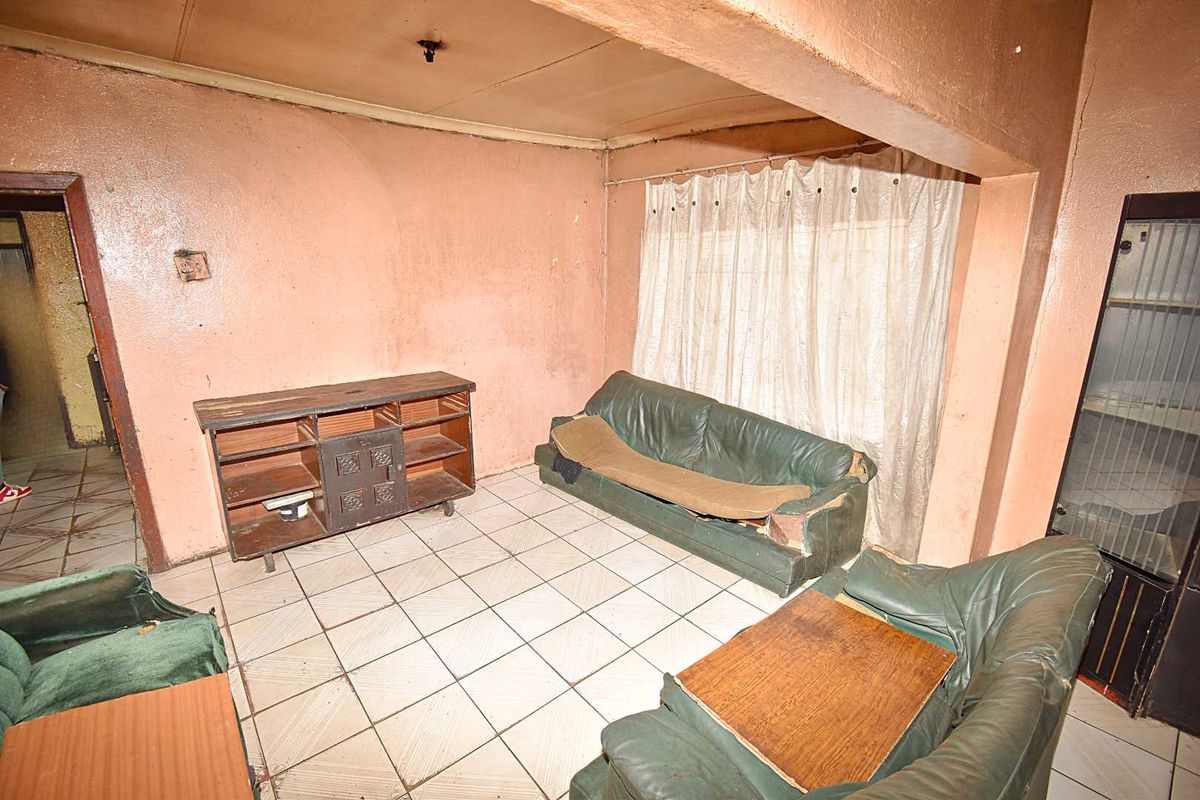 A dated living room featuring ceramic floor tiles and a built-in display cabinet, requiring significant cosmetic updates and wall repairs.