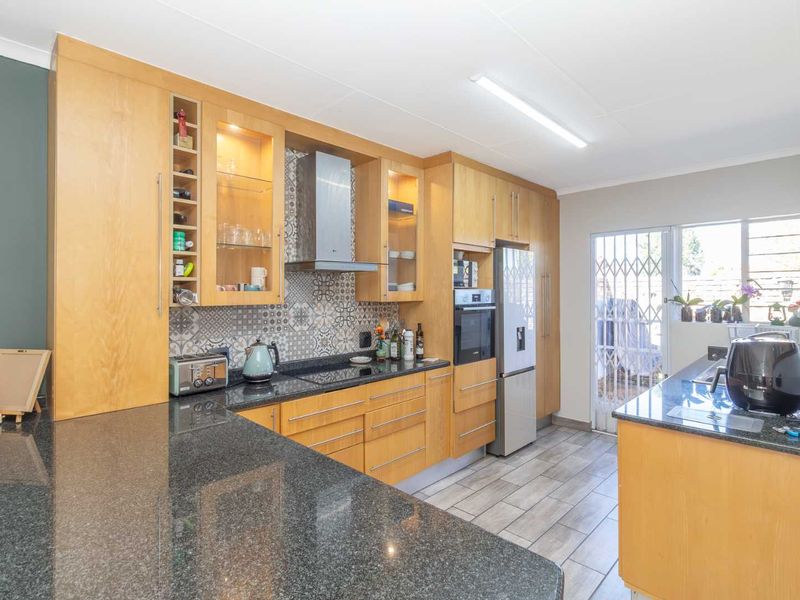 A well-maintained kitchen featuring wooden cabinetry, granite countertops, a decorative tile backsplash, and integrated appliances, with direct access to an outdoor area.