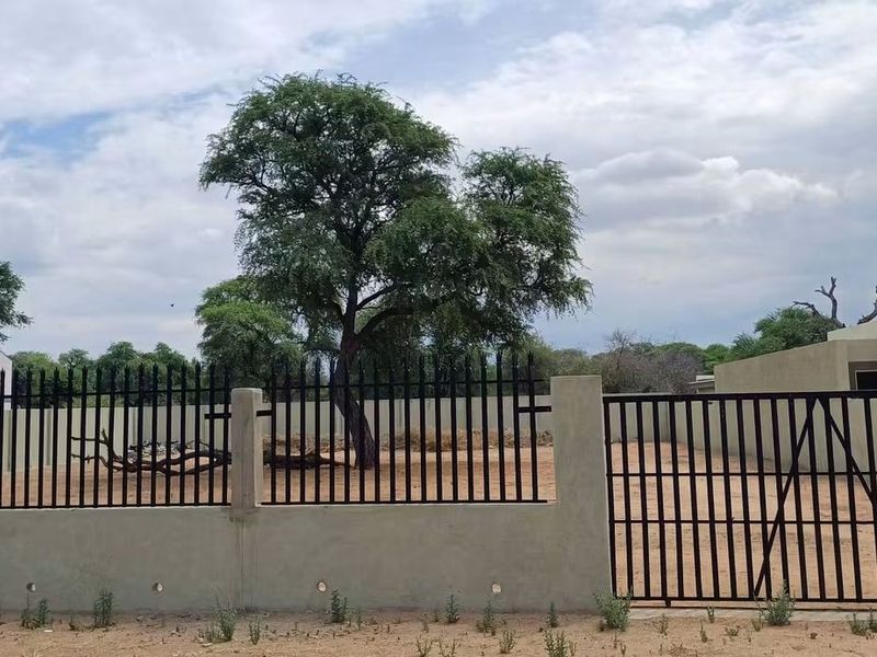 A view of a vacant residential plot featuring a secure perimeter wall, metal fencing, and a gated entrance.