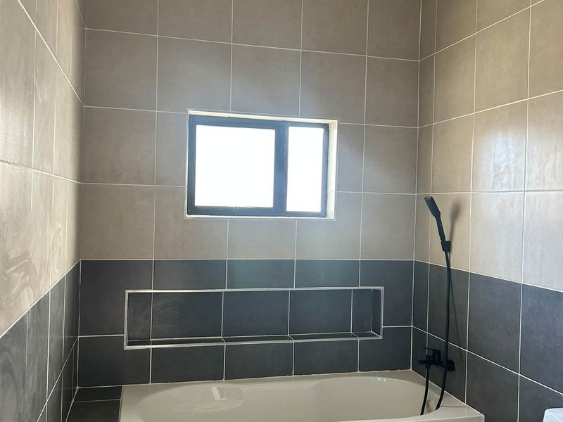 A modern bathroom featuring a built-in bathtub with a recessed wall niche, handheld shower fixture, and contemporary dual-tone ceramic wall tiling.