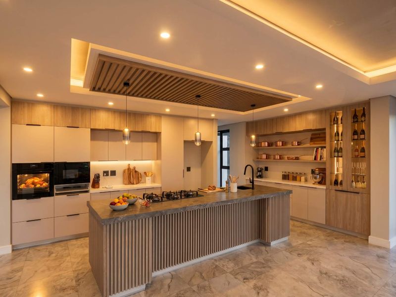 Modern luxury kitchen featuring a large central island, integrated appliances, custom slatted timber ceiling detail, and high-end cabinetry with ambient lighting.