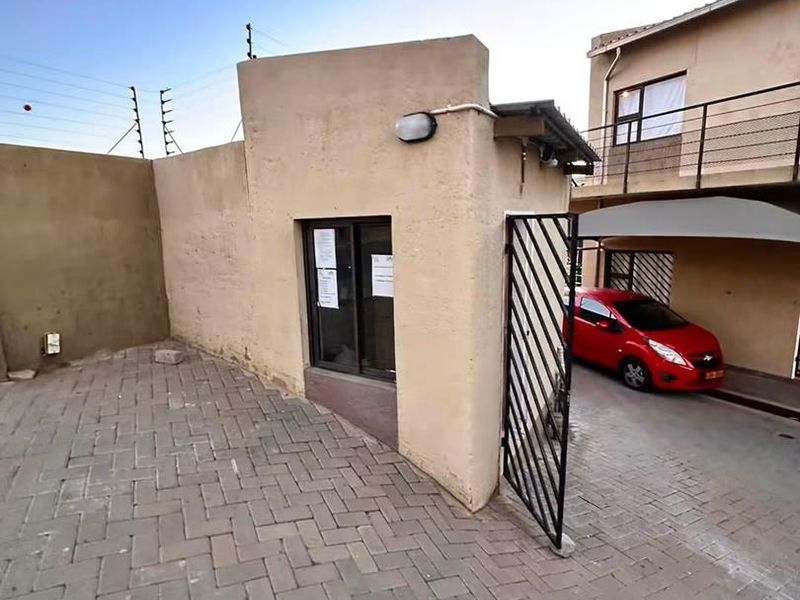 Front exterior view of the apartment complex featuring a paved driveway, security gate, and carport parking area.