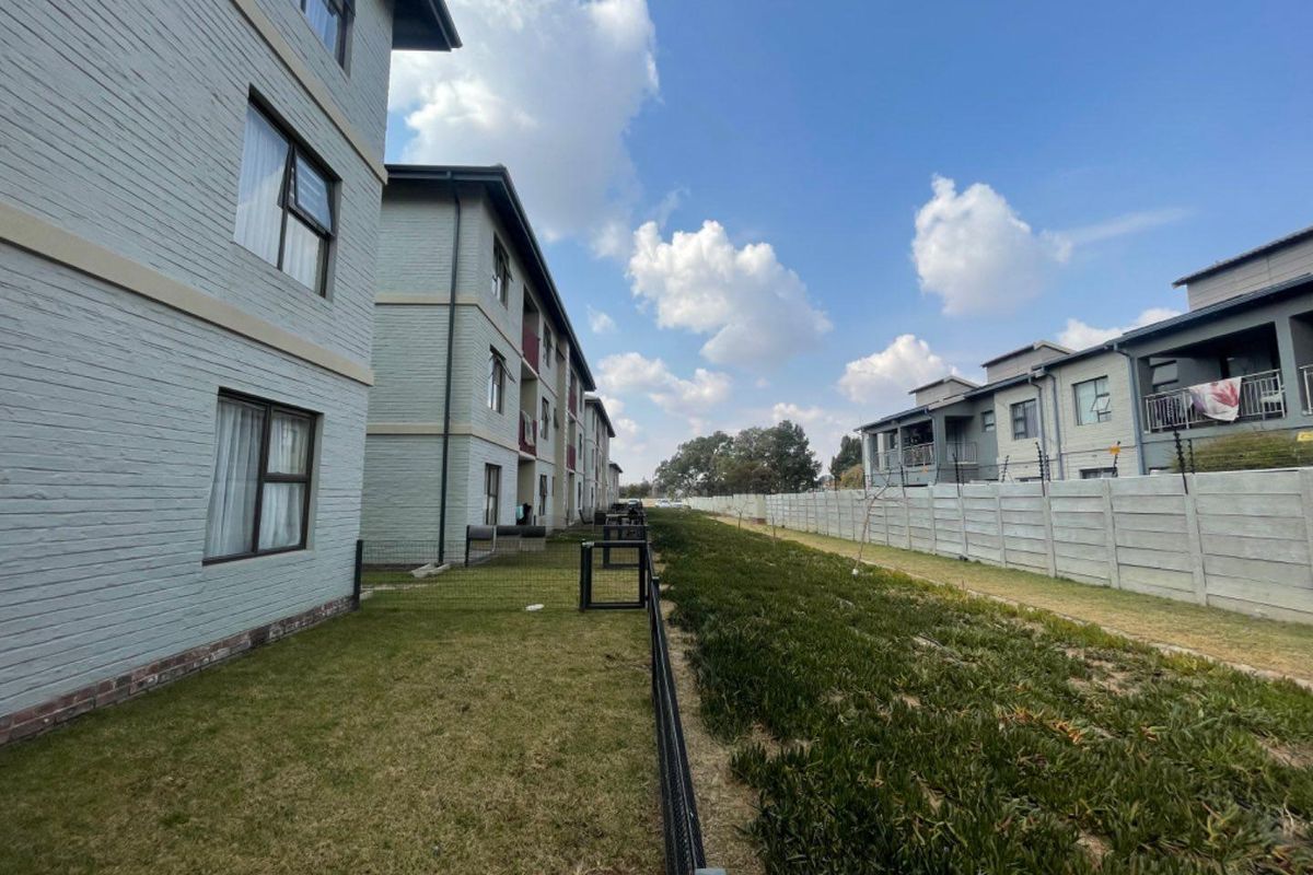 Exterior view of the apartment complex showing the rear facade, landscaped lawn area, and secure boundary wall with electric fencing.