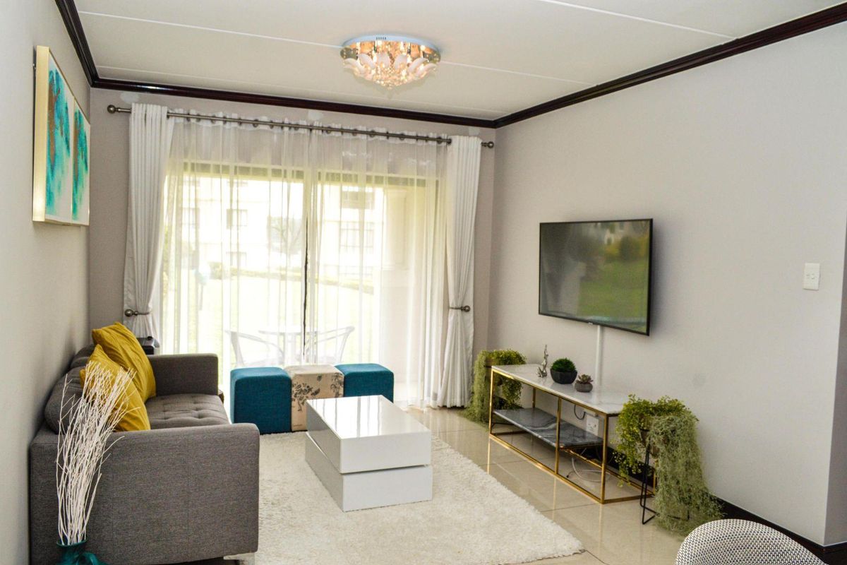 A well-maintained living room featuring tiled flooring, a decorative ceiling light, and a large sliding glass door providing access to the patio.