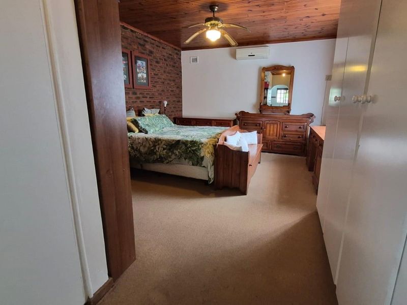 Spacious bedroom featuring an exposed brick feature wall, timber ceiling, ceiling fan, split-system air conditioning, and ample built-in cupboard storage.