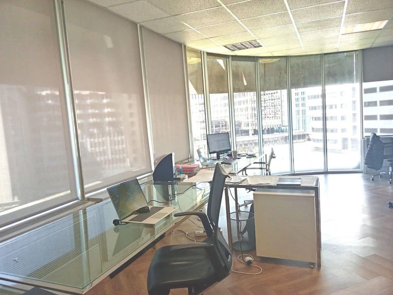 A bright office space featuring parquet flooring, a suspended ceiling, and expansive floor-to-ceiling windows offering natural light and city views.