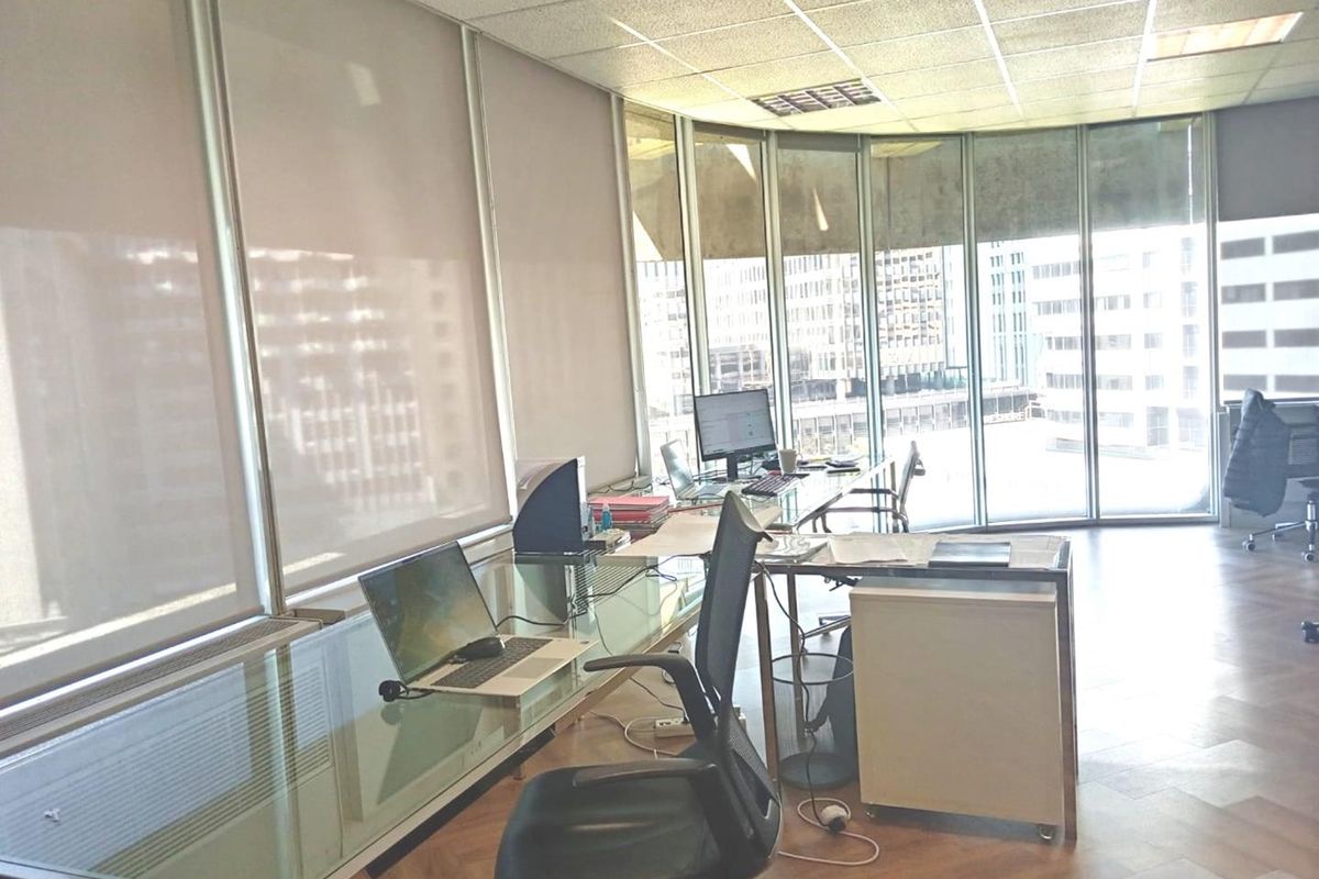 A bright office space featuring parquet flooring, a suspended ceiling, and expansive floor-to-ceiling windows offering natural light and city views.