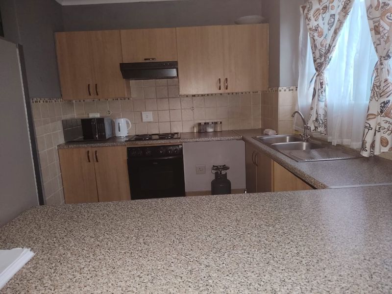 Functional kitchen featuring laminate cabinetry, granite-look countertops, built-in oven with hob, extractor fan, and a double bowl stainless steel sink.