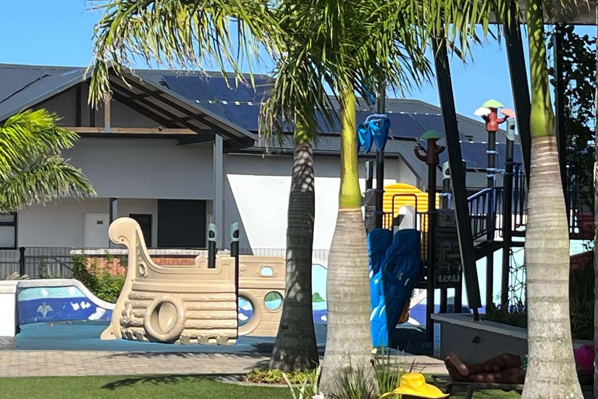 A well-maintained outdoor communal area featuring a children's playground, paved patio space, and solar panels installed on the adjacent building roof.