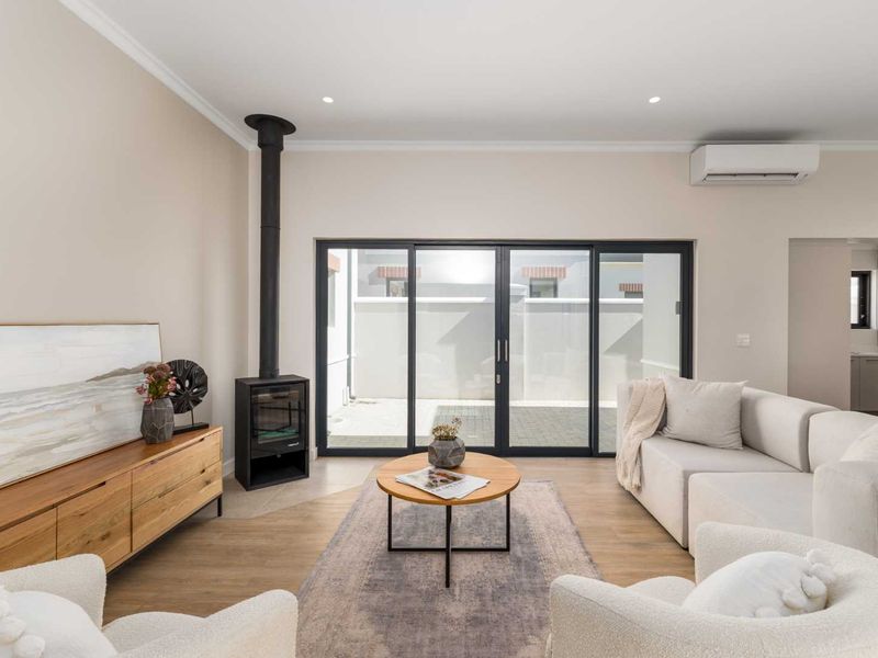 A bright and modern living room featuring a sleek freestanding fireplace, large sliding glass doors leading to the patio, and split system air conditioning.