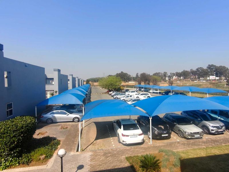 An elevated view of the townhouse complex exterior, featuring paved parking areas covered by blue shade cloth structures.