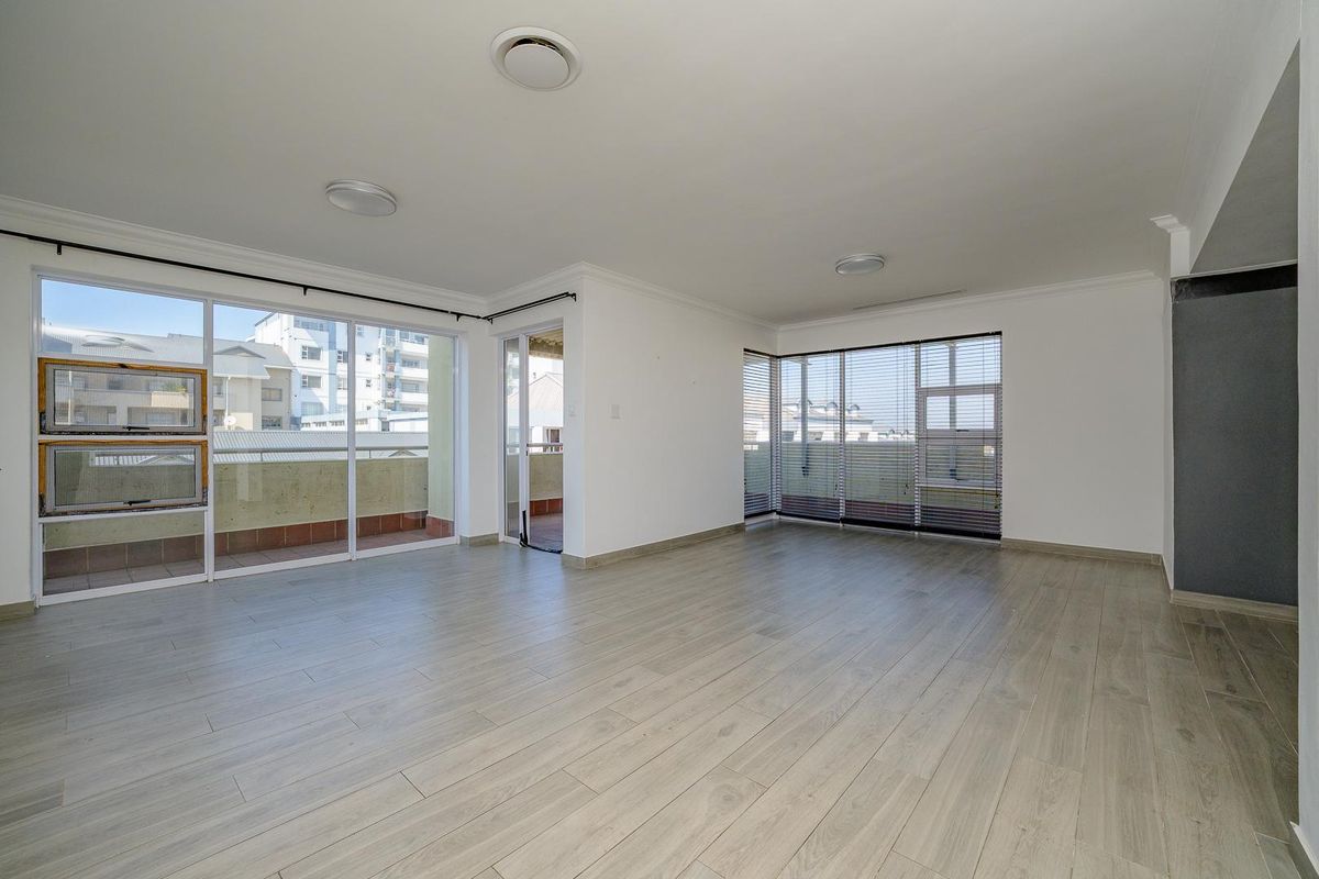 Spacious, light-filled living area featuring modern laminate flooring, large sliding glass doors leading to a balcony, and neutral finishes throughout.