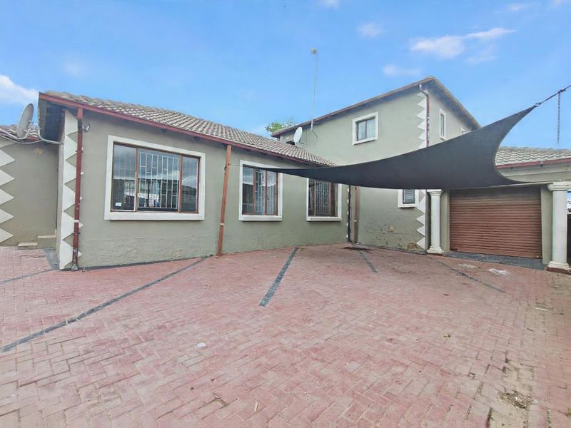 Front exterior view of the house featuring a paved driveway, roller garage door, and security bars on the windows.