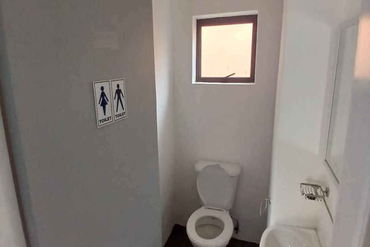 A compact bathroom featuring a white pedestal basin, a standard toilet, and a small window, finished with neutral walls and dark flooring.