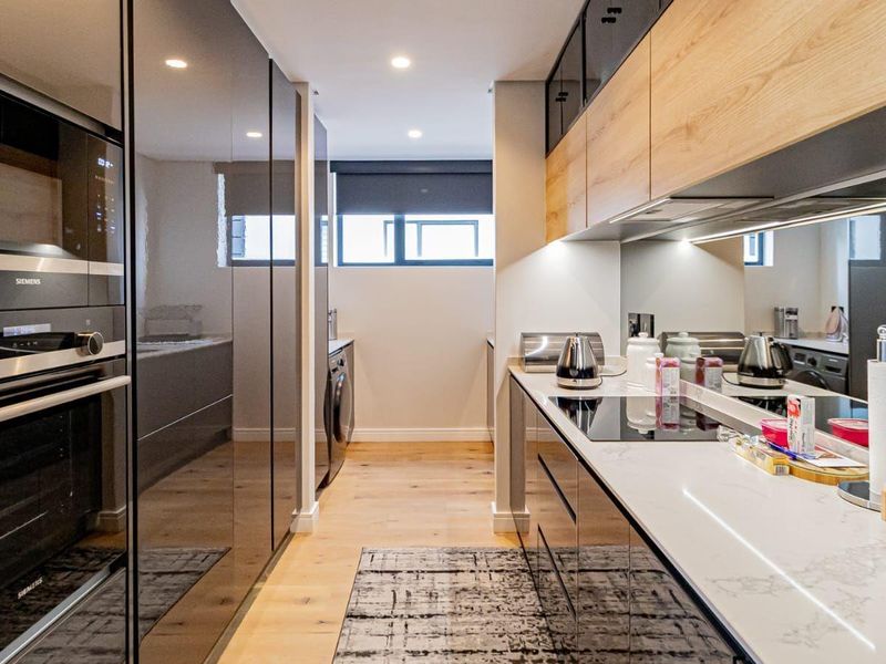 Modern galley-style kitchen featuring high-end integrated Siemens appliances, sleek cabinetry, stone countertops, and a mirror splashback with warm recessed lighting.