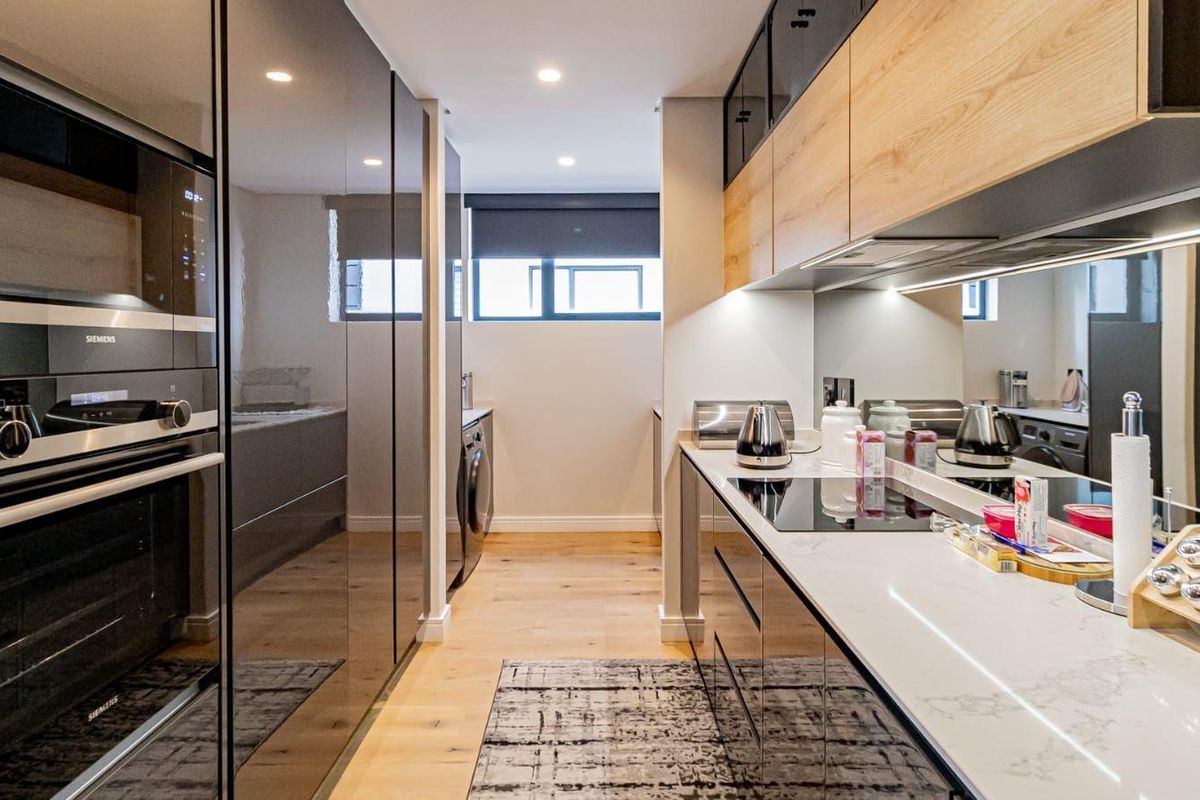 Modern galley-style kitchen featuring high-end integrated Siemens appliances, sleek cabinetry, stone countertops, and a mirror splashback with warm recessed lighting.